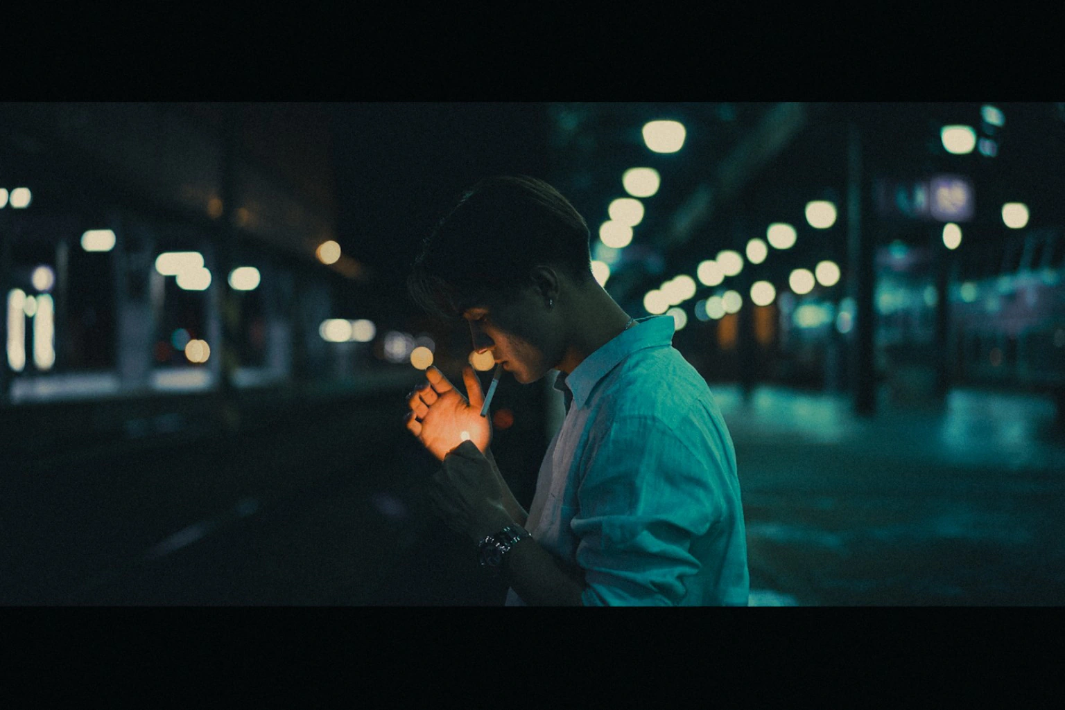 Young man lighting a cigarette at night under teal lights