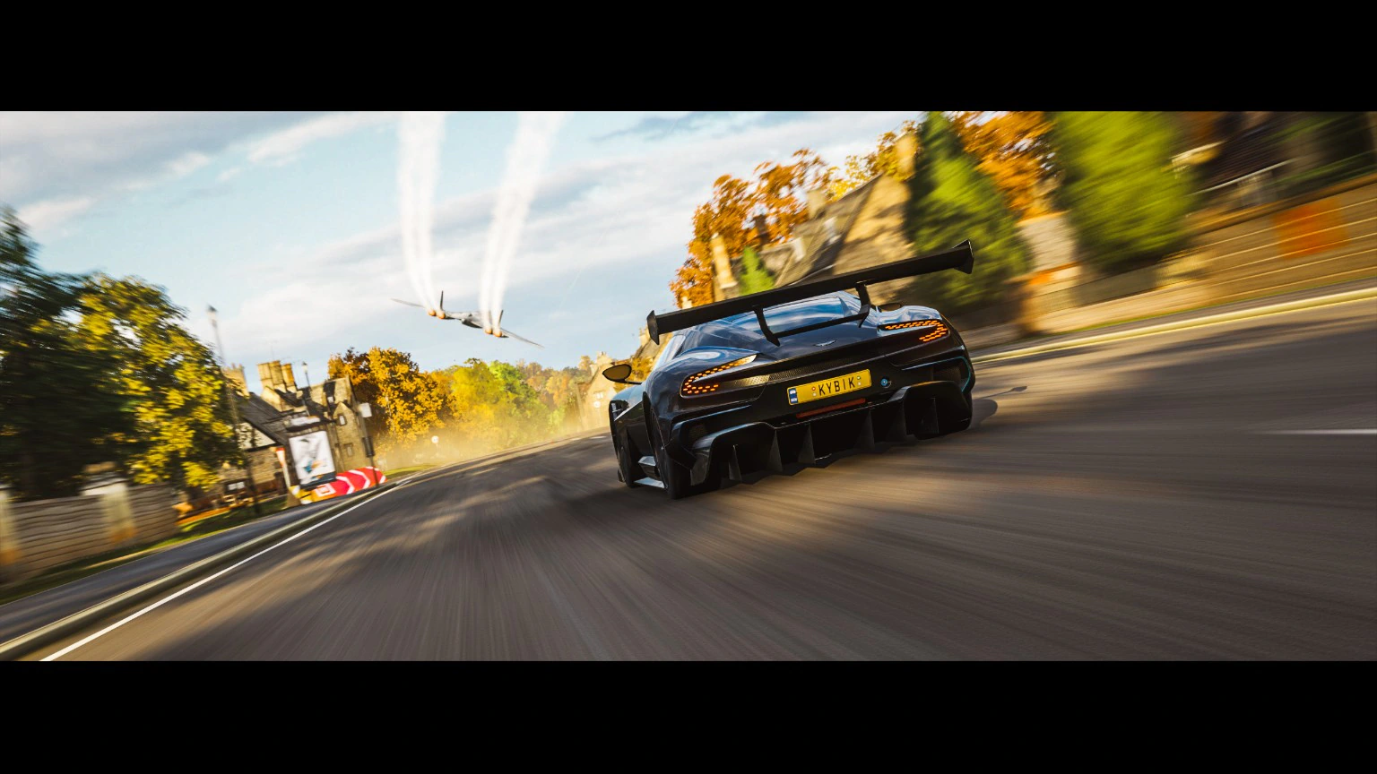 Track car speeding through a bright autumn landscape with a jet overhead