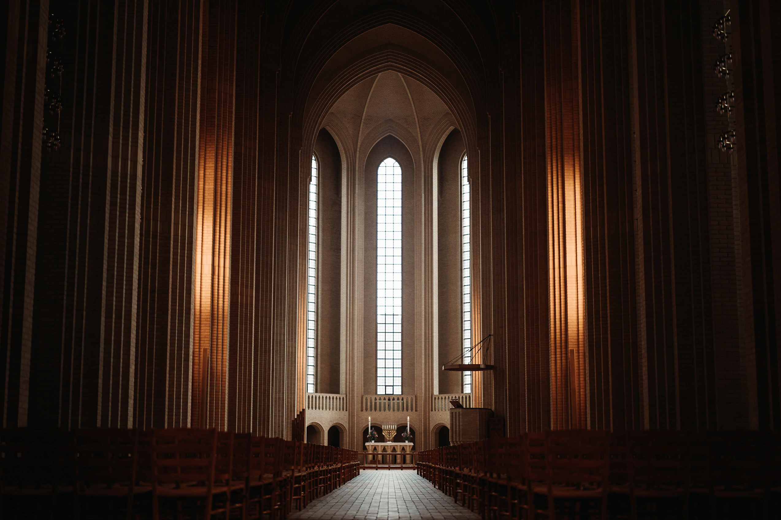 The altar and three tall windows centred between glowing brick columns