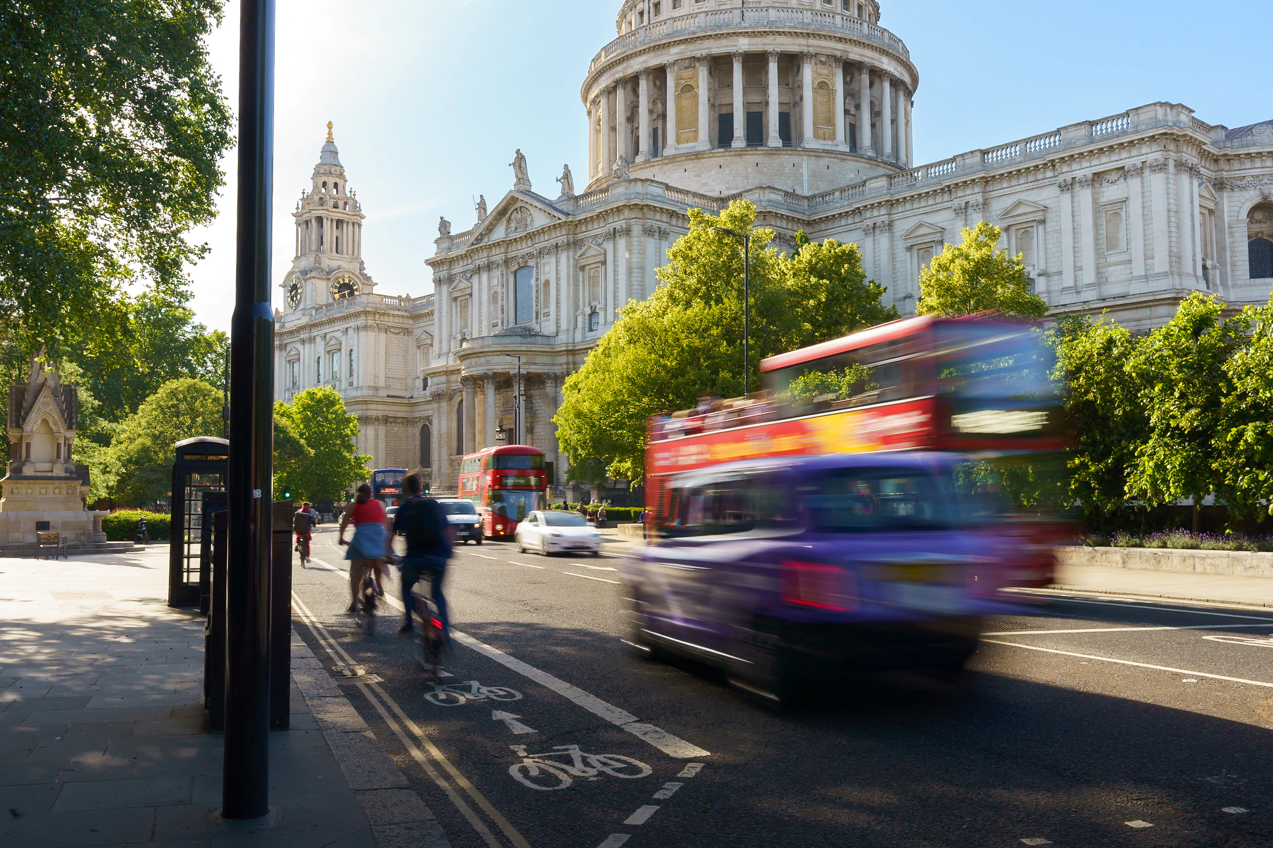 A red double-decker bus passing St Paul's Cathedral in bright sunlight