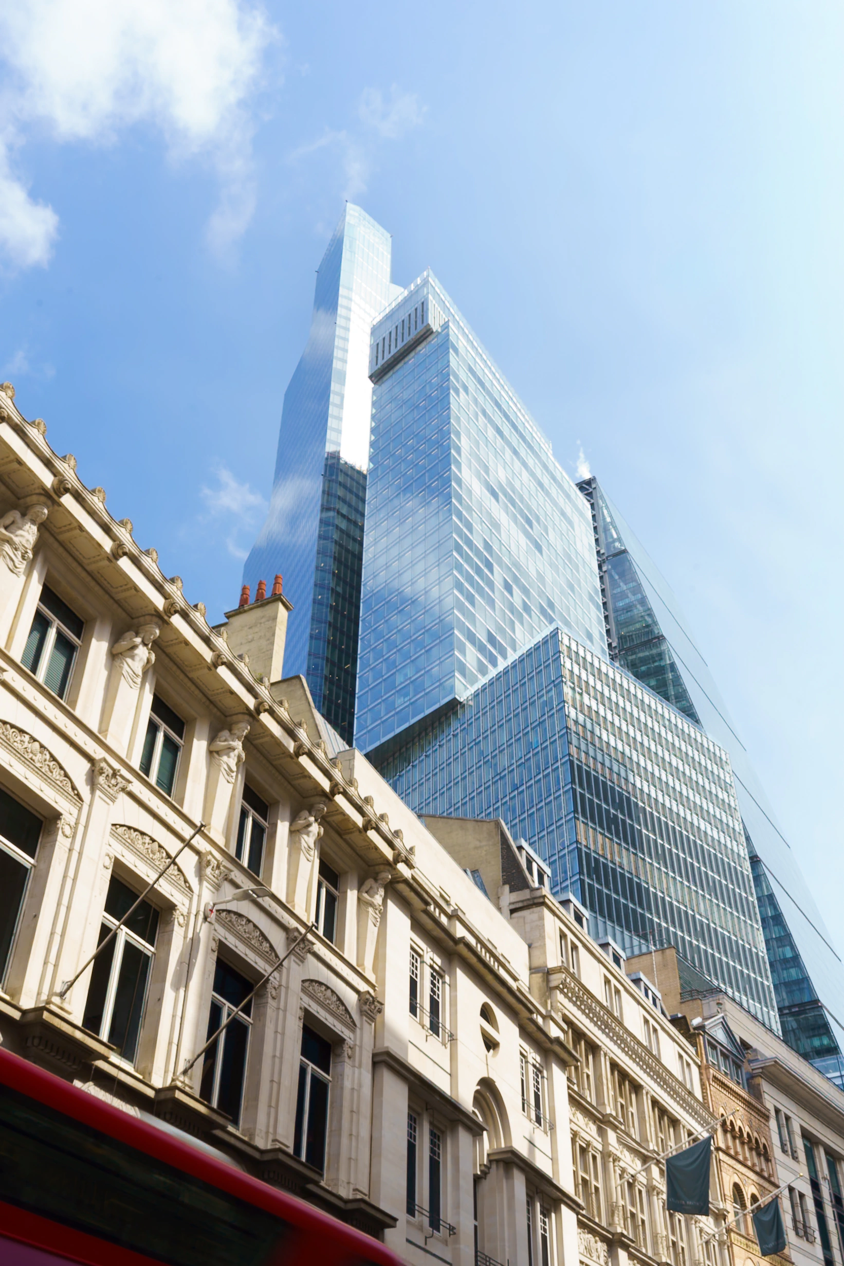 Modern glass towers rising above older London buildings beneath a clear blue sky