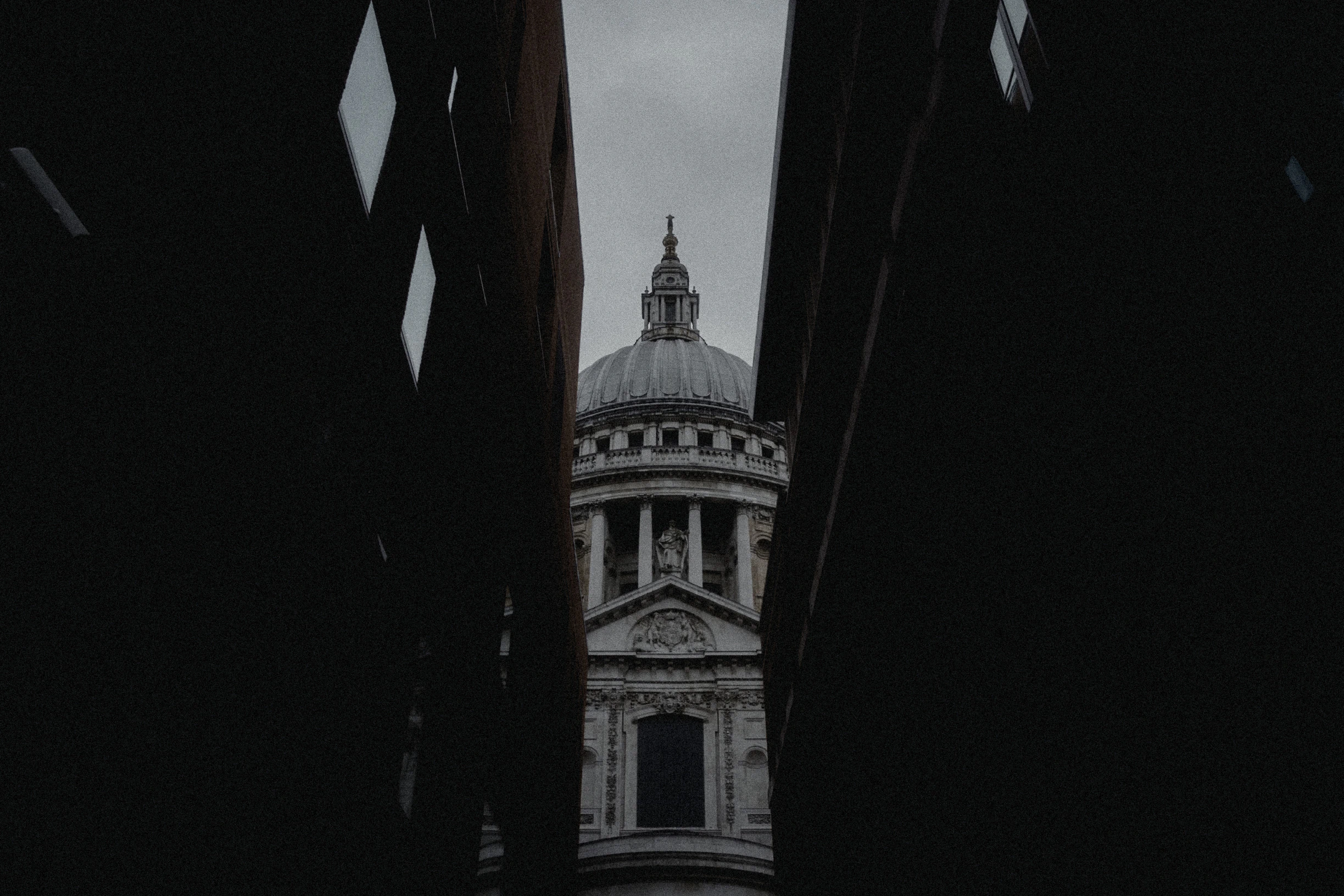 St Paul's Cathedral framed between dark London buildings beneath a grey sky
