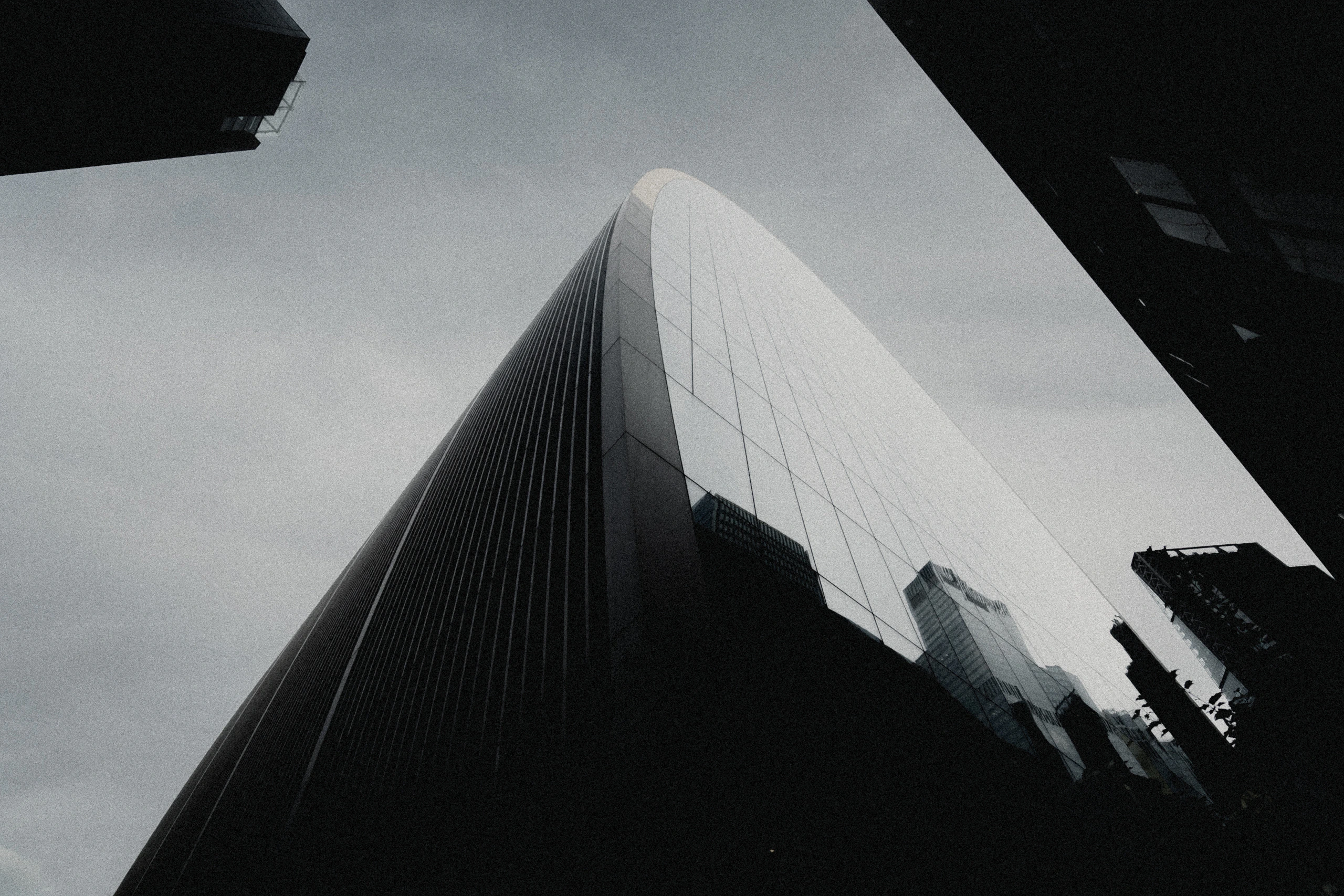 A pale modern London tower rising into an overcast sky between dark buildings