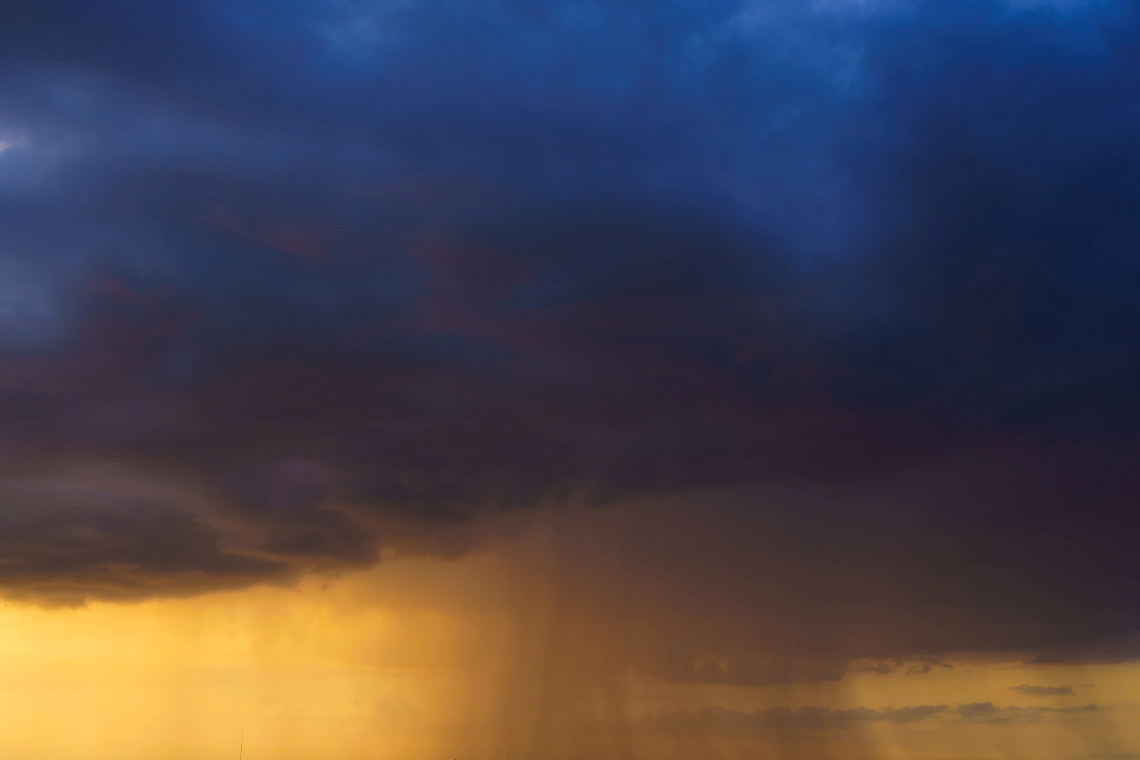 Storm cloud and a golden rain shaft at sunset