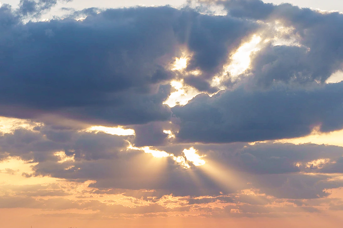 Golden sunlight streaming through breaks in a dark cloud bank
