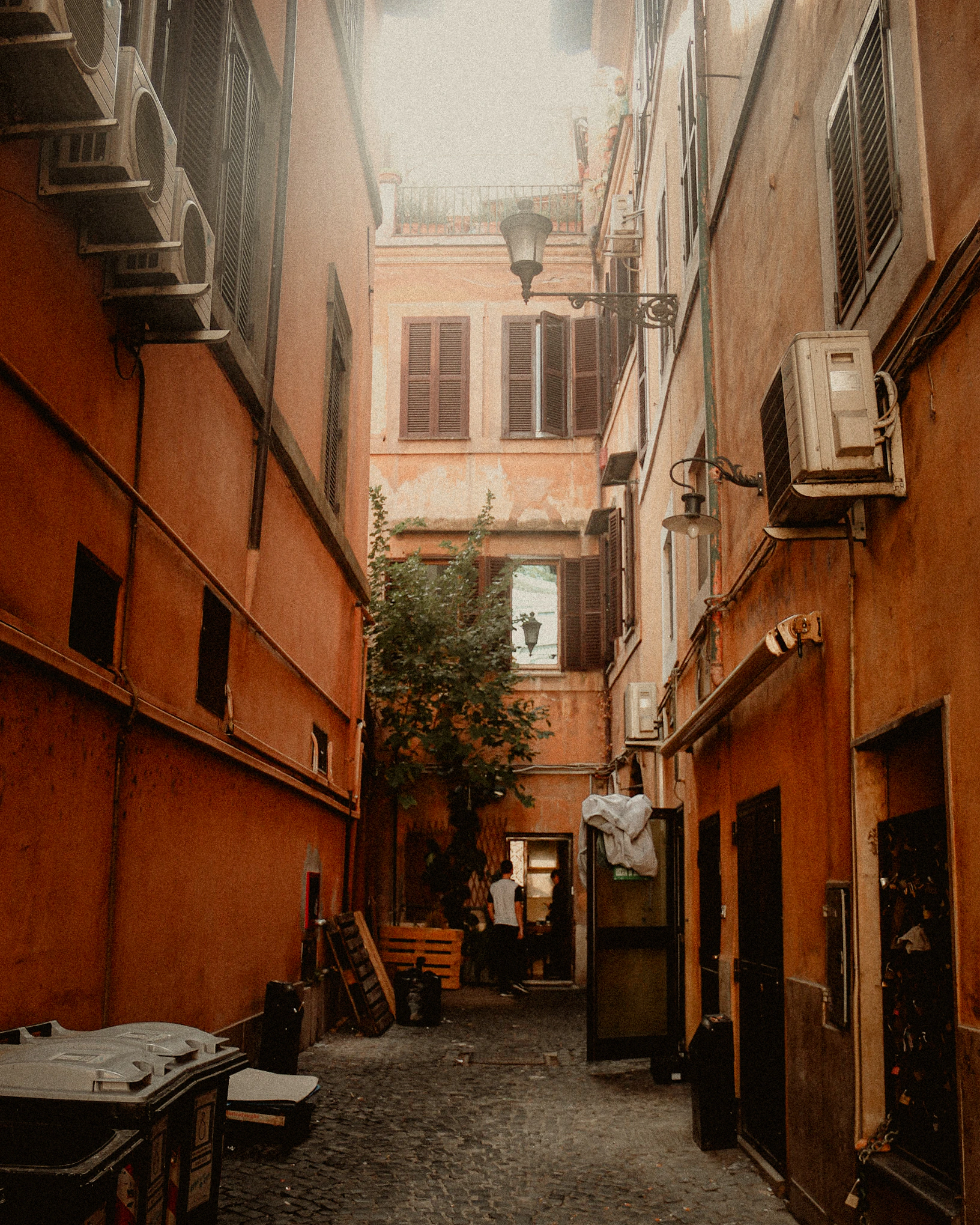 A narrow Roman courtyard passage enclosed by orange buildings