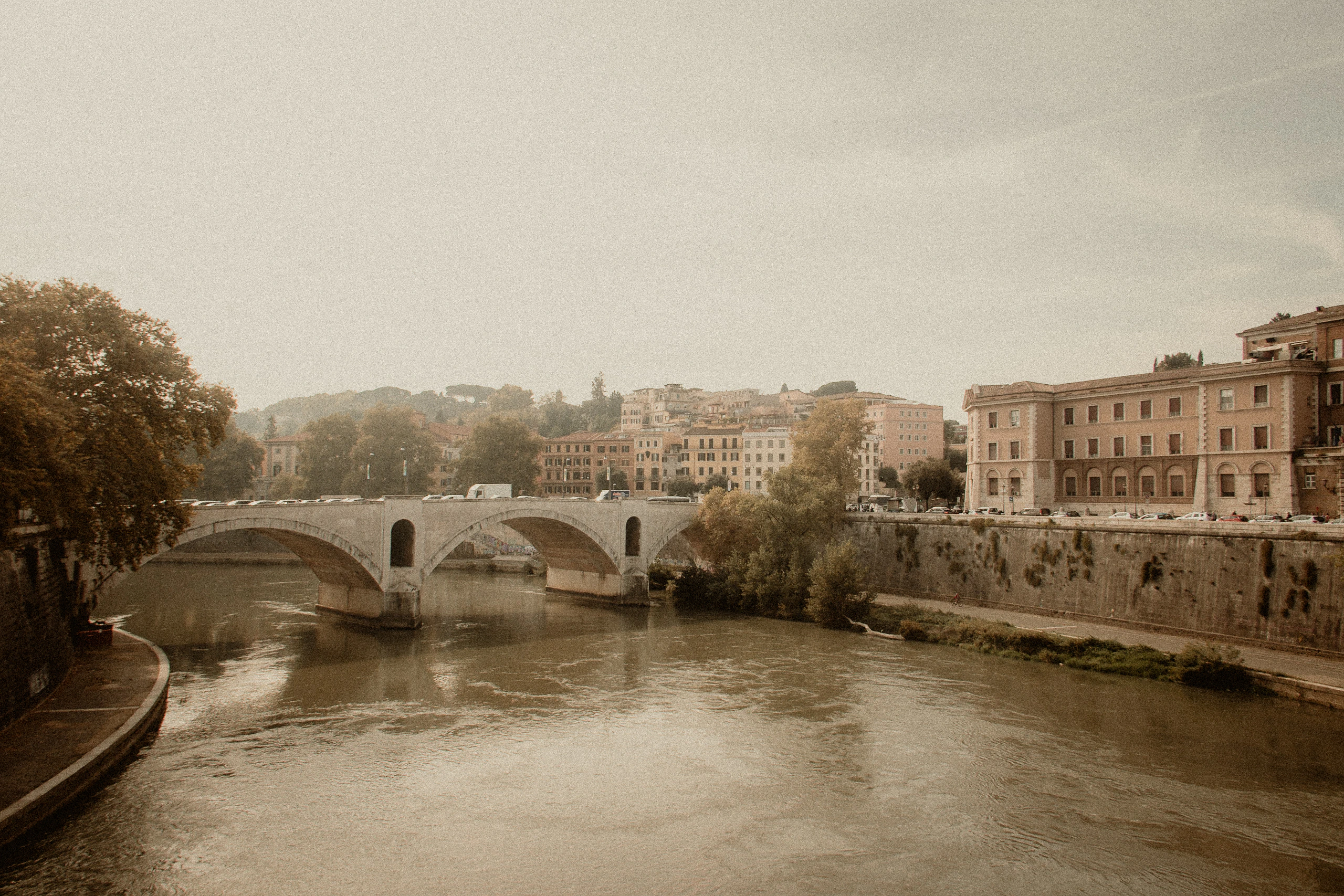 The Tiber flowing beneath a stone bridge in warm hazy light