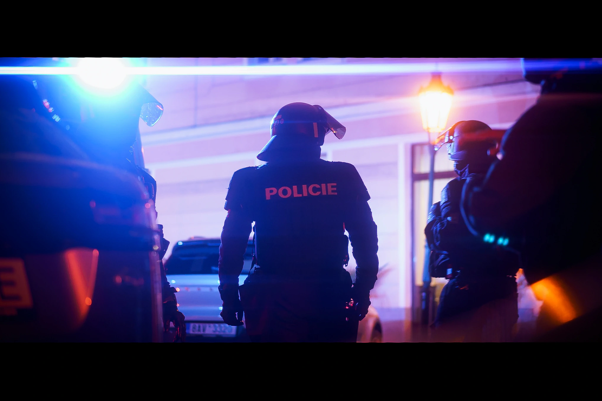Police officers in silhouette between blue emergency lights and a warm street lamp