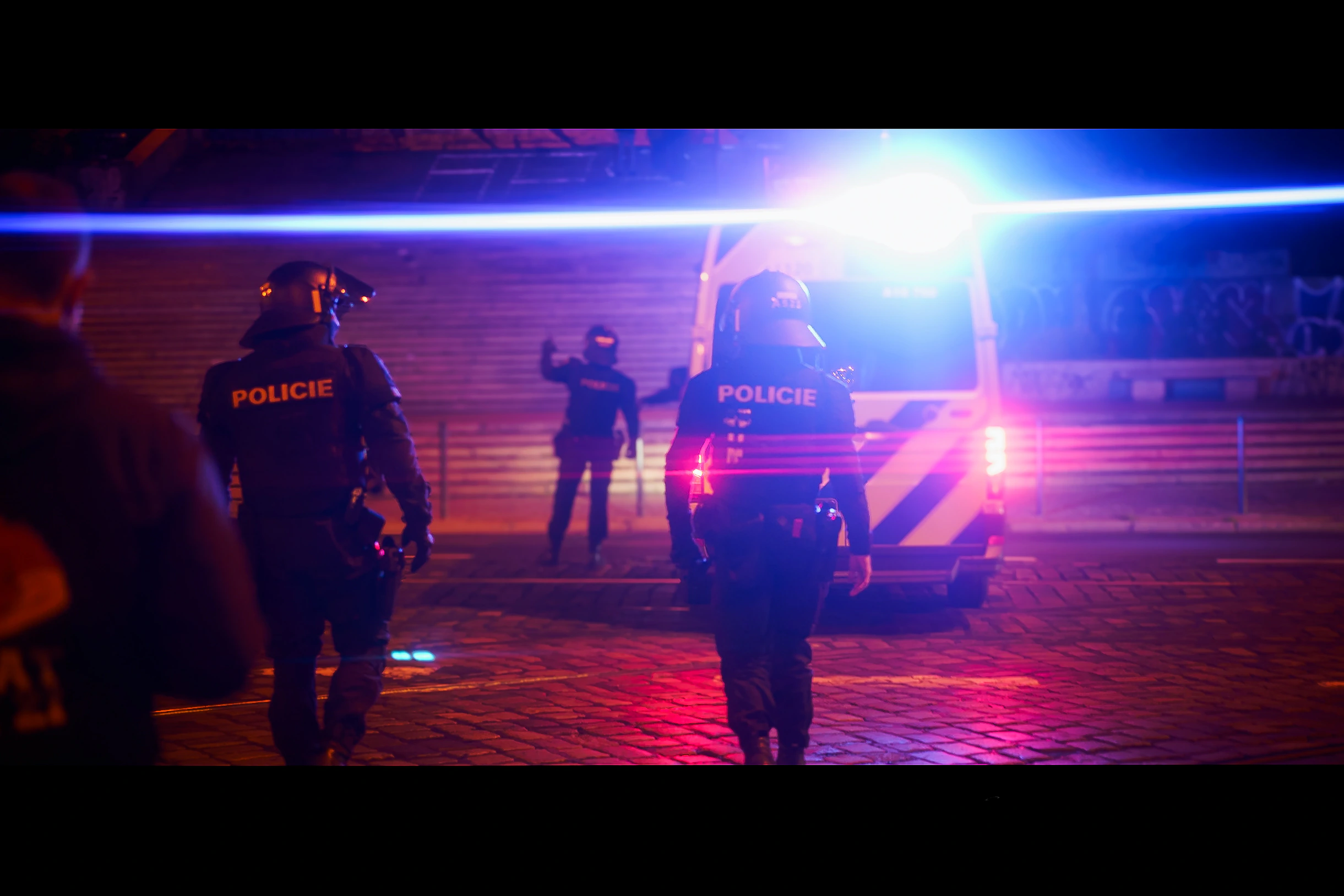 Two police officers walking towards a van through blue and magenta emergency light