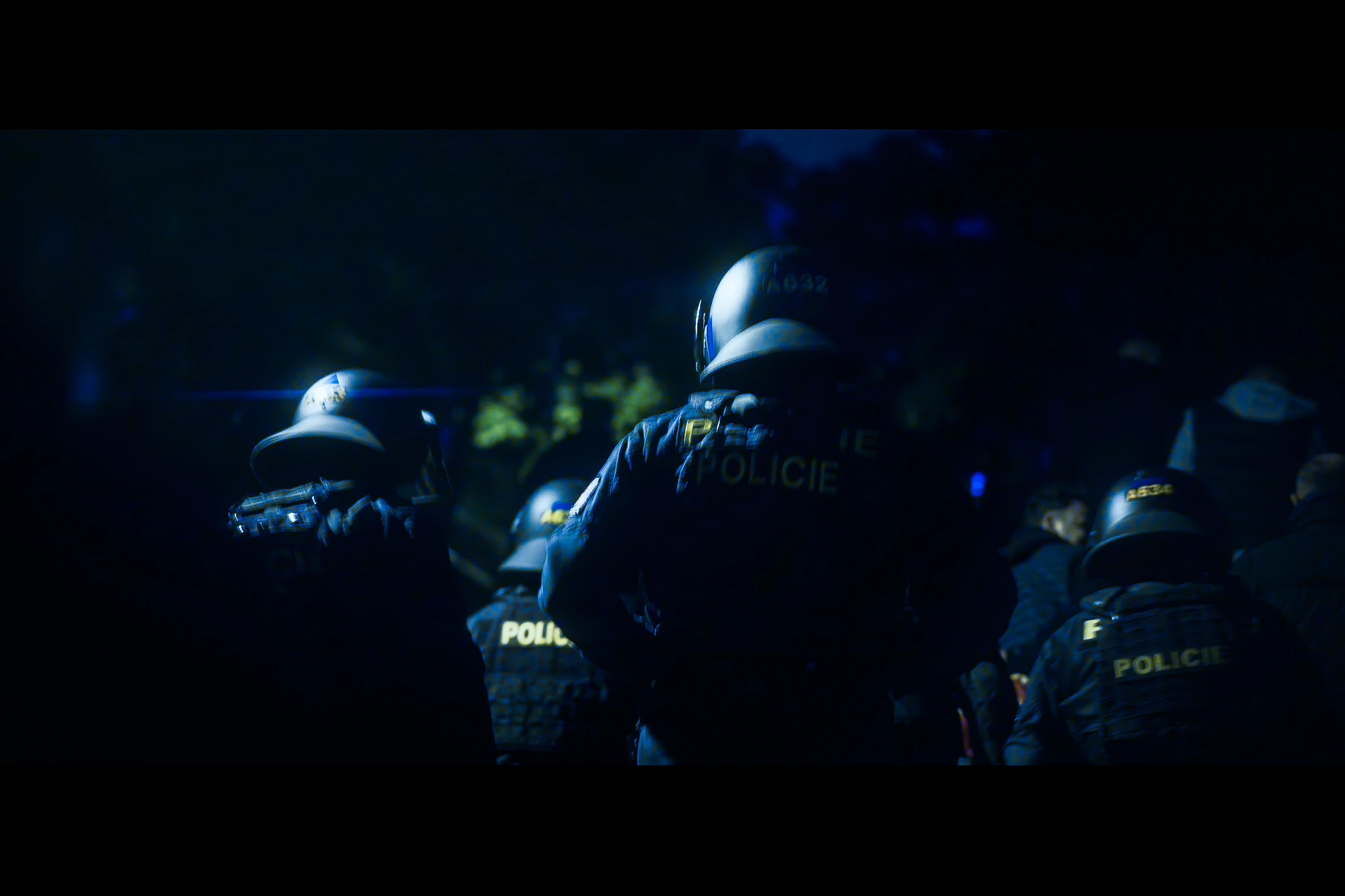 A dense group of police officers in riot helmets moving through darkness