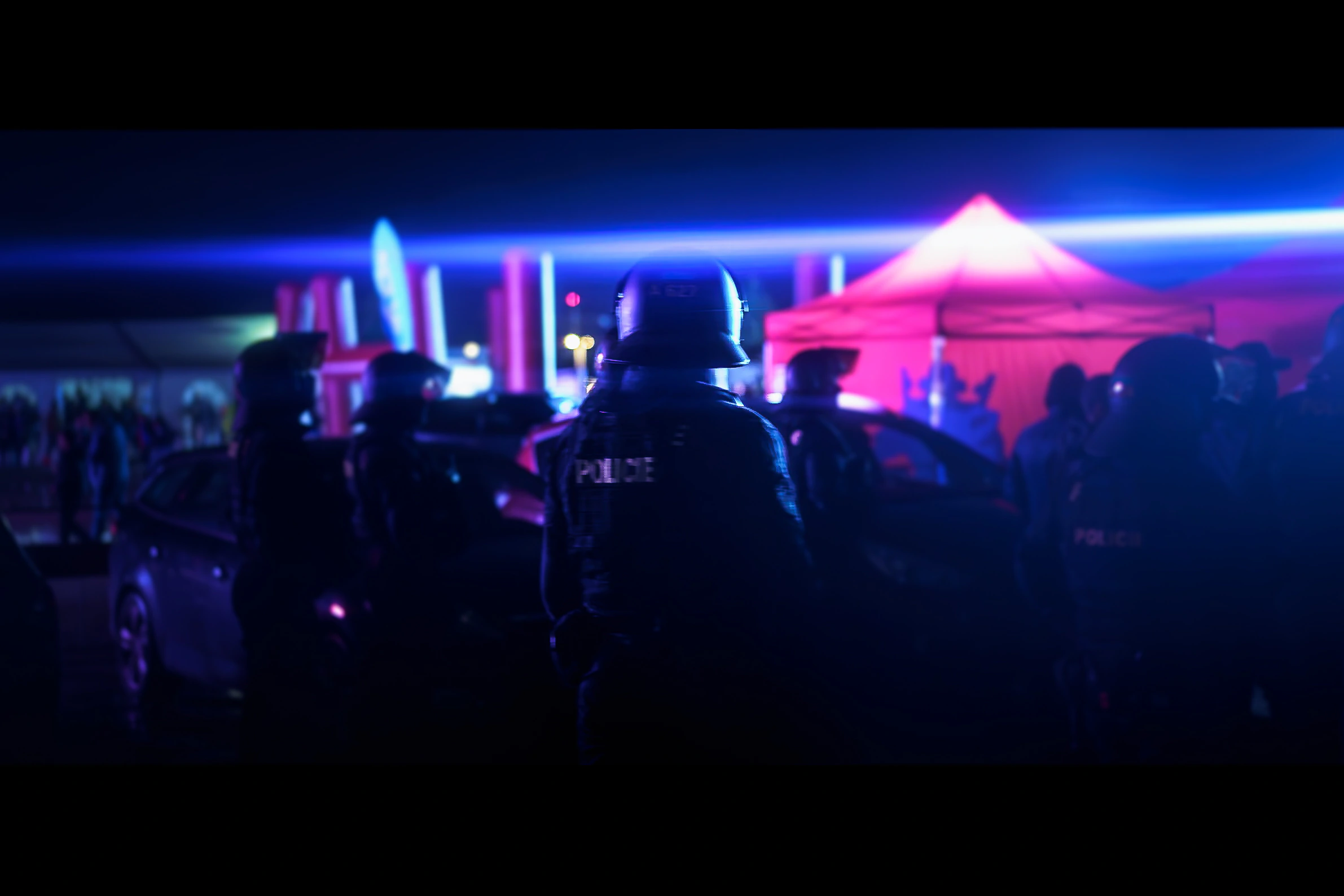 Police officers gathered beside red tents beneath a blue line of light