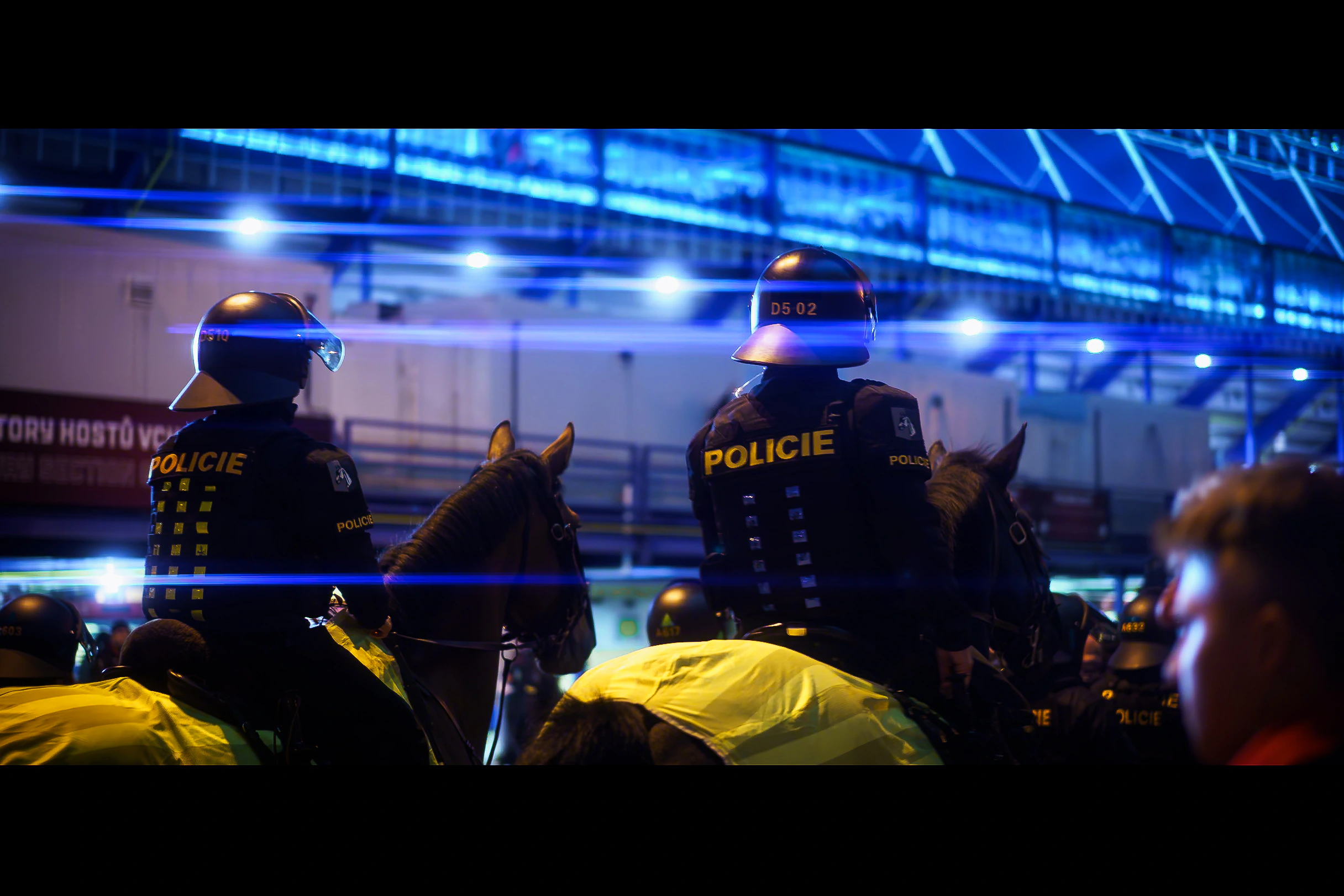 Mounted police officers surrounded by a crowd beneath blue lights