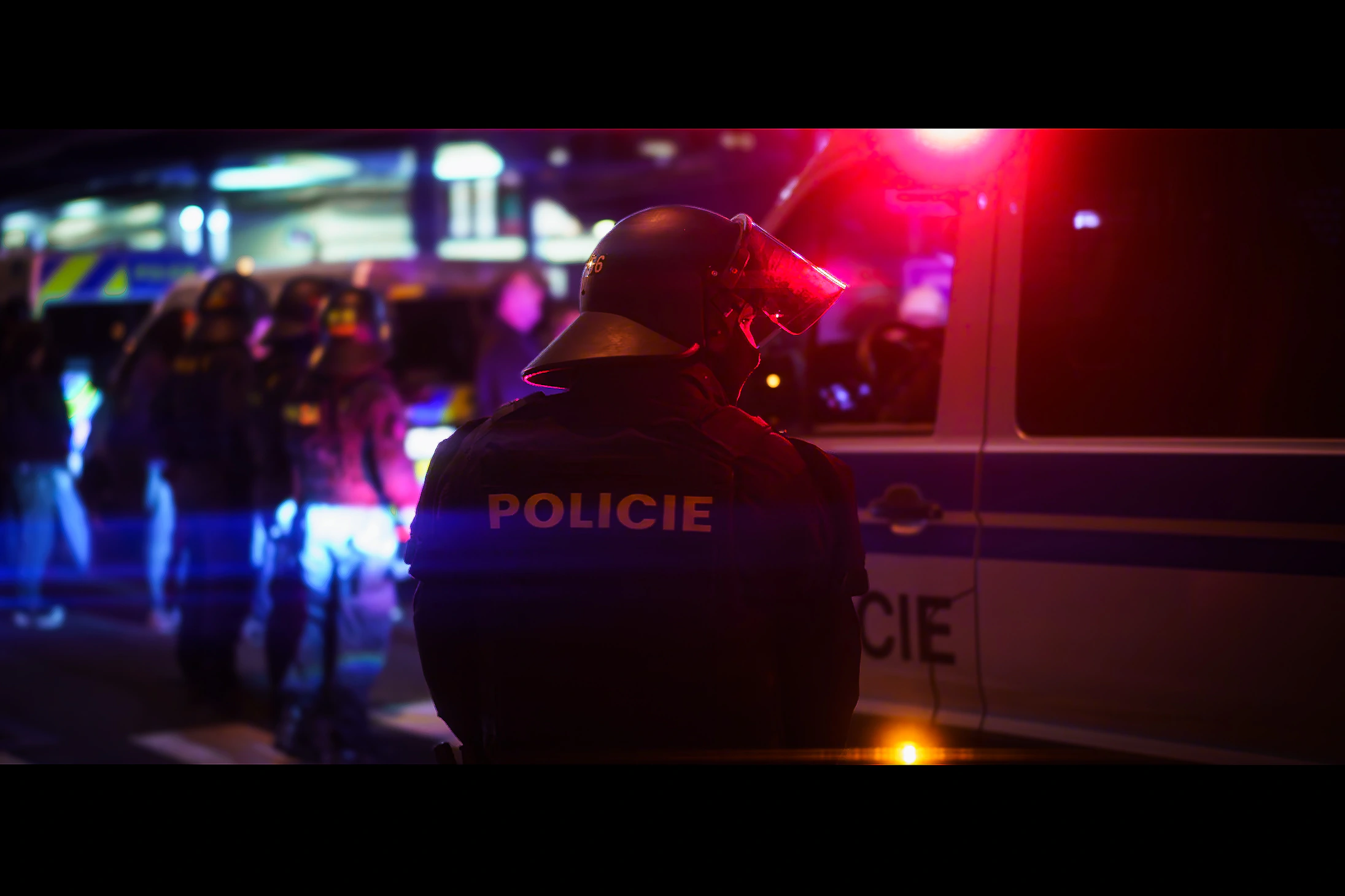 A police officer standing in red and blue light beside police vehicles