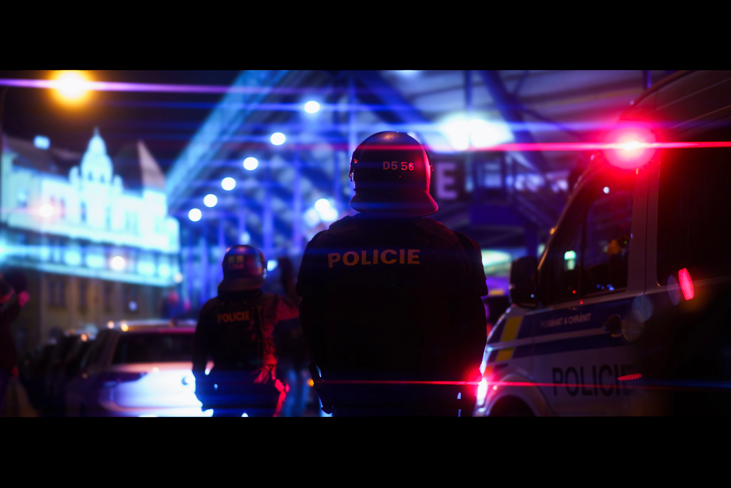 A police officer standing between vans beneath red and blue emergency lights