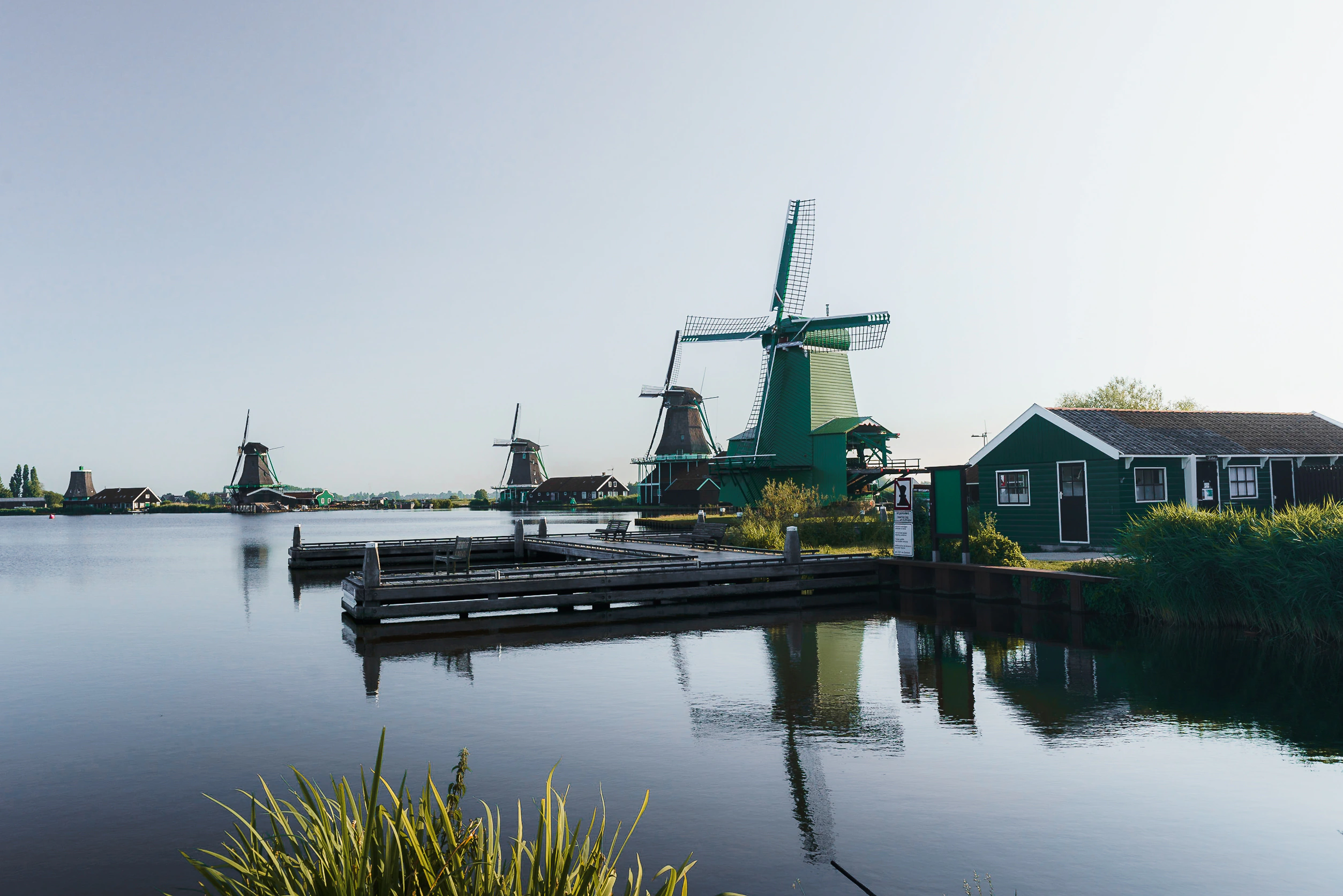Several windmills and green wooden buildings gathered along the water