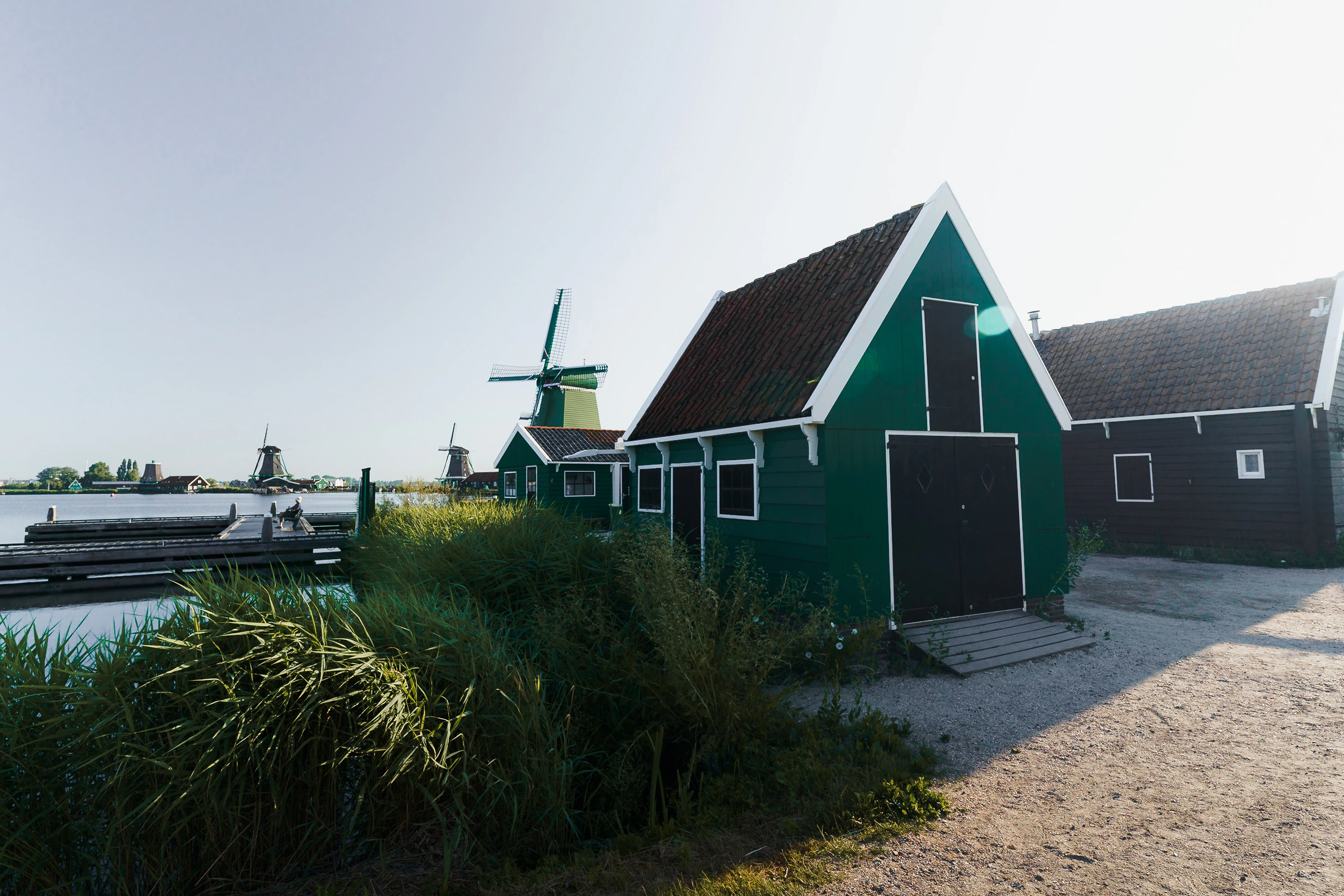 Green wooden barns with windmills rising behind them at Zaanse Schans