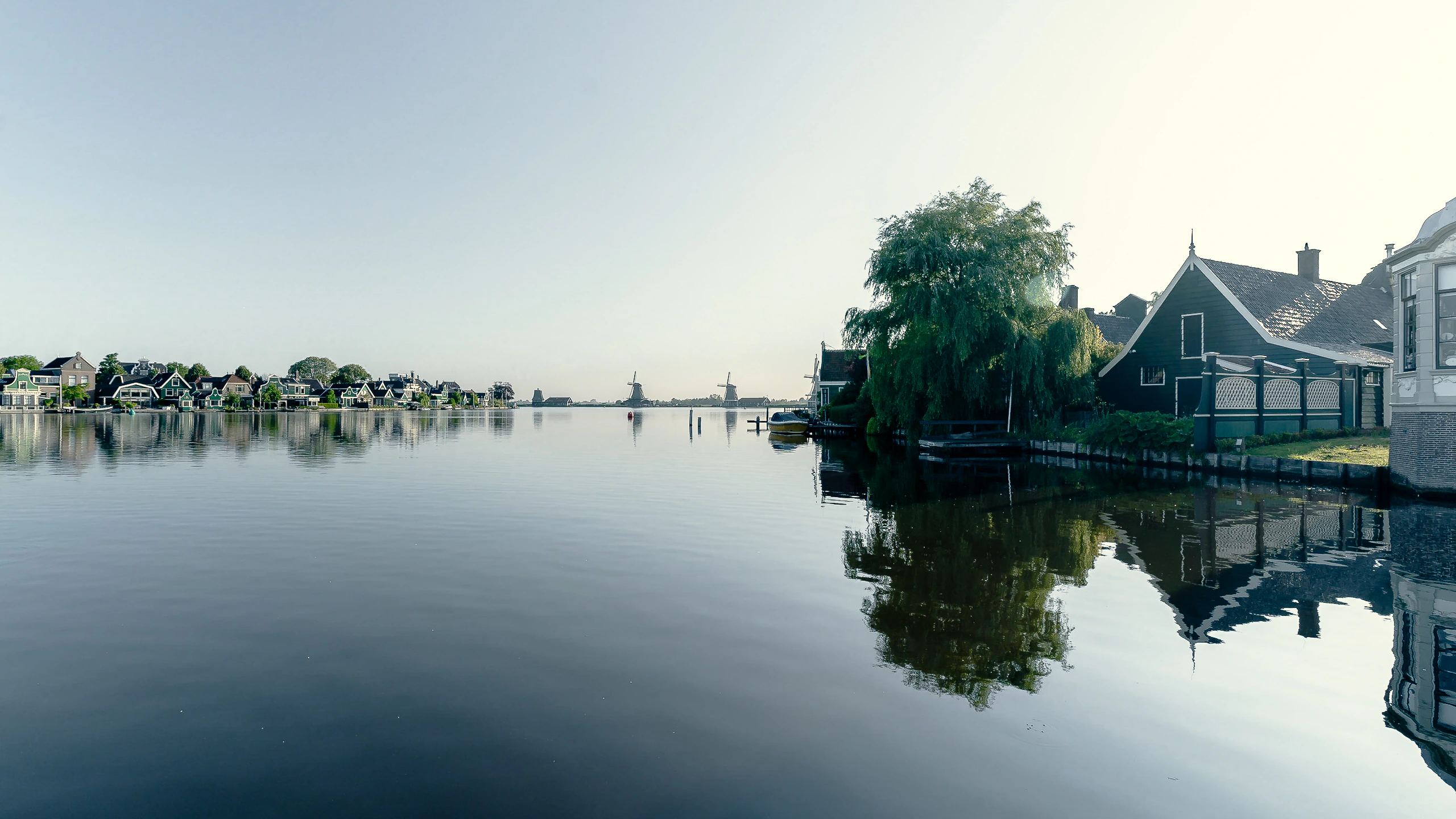 A broad reflective river view with village houses and windmills in the distance