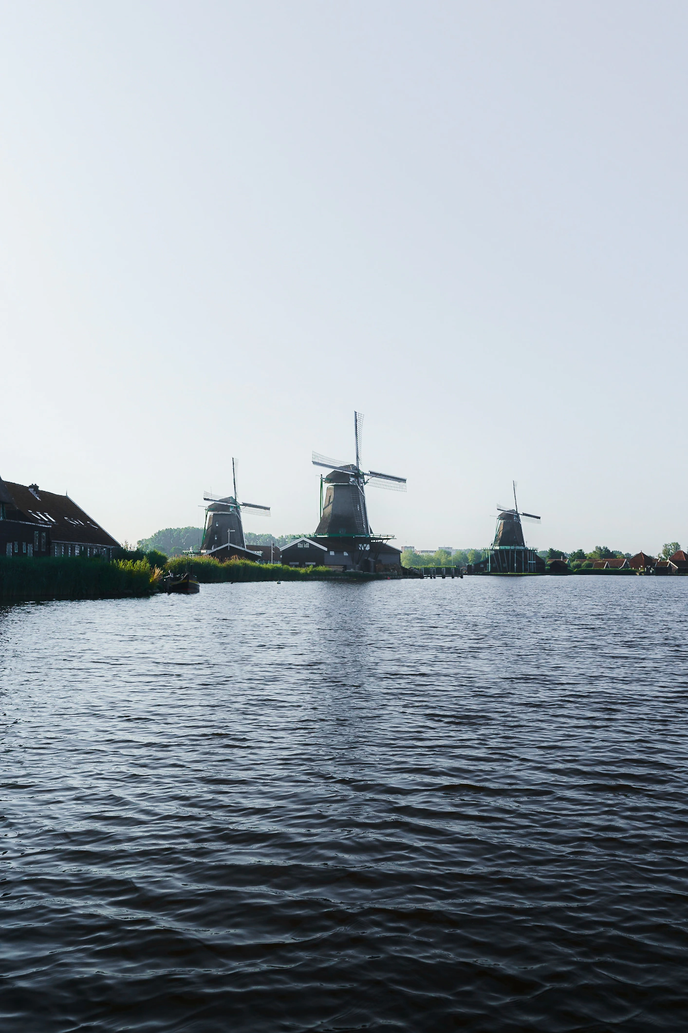 Windmills beyond rippled water beneath an immense pale sky