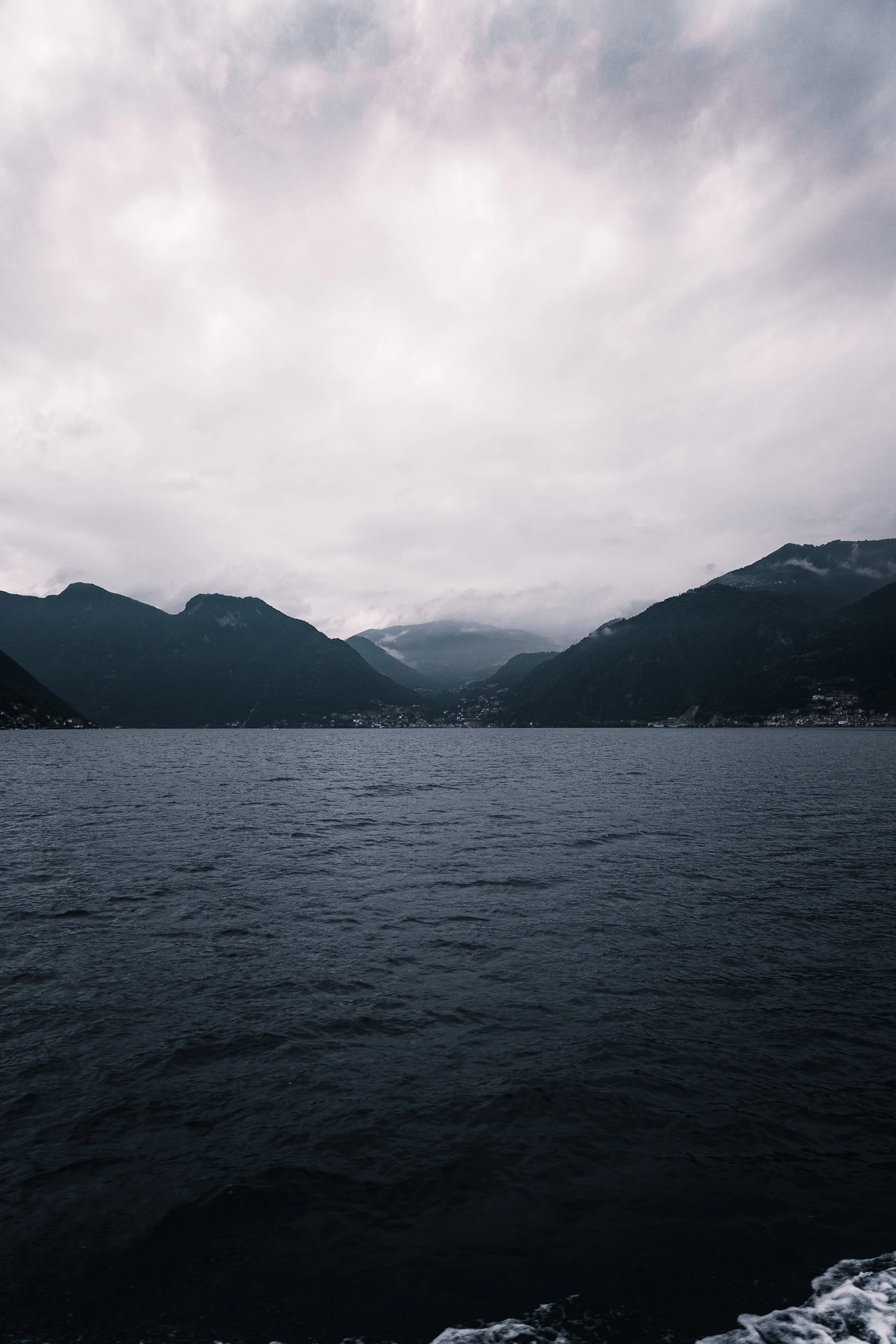 A vertical view across dark water towards cloud-covered mountains