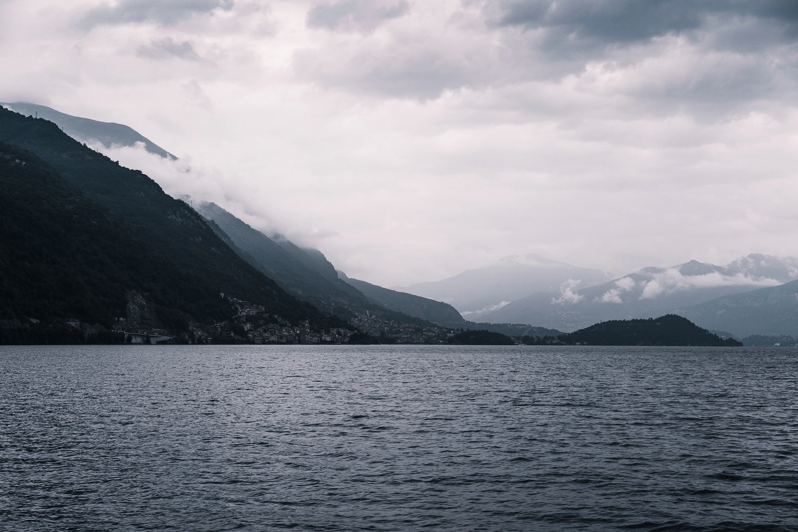 Lake Como beneath layered storm clouds and mist-filled mountain valleys