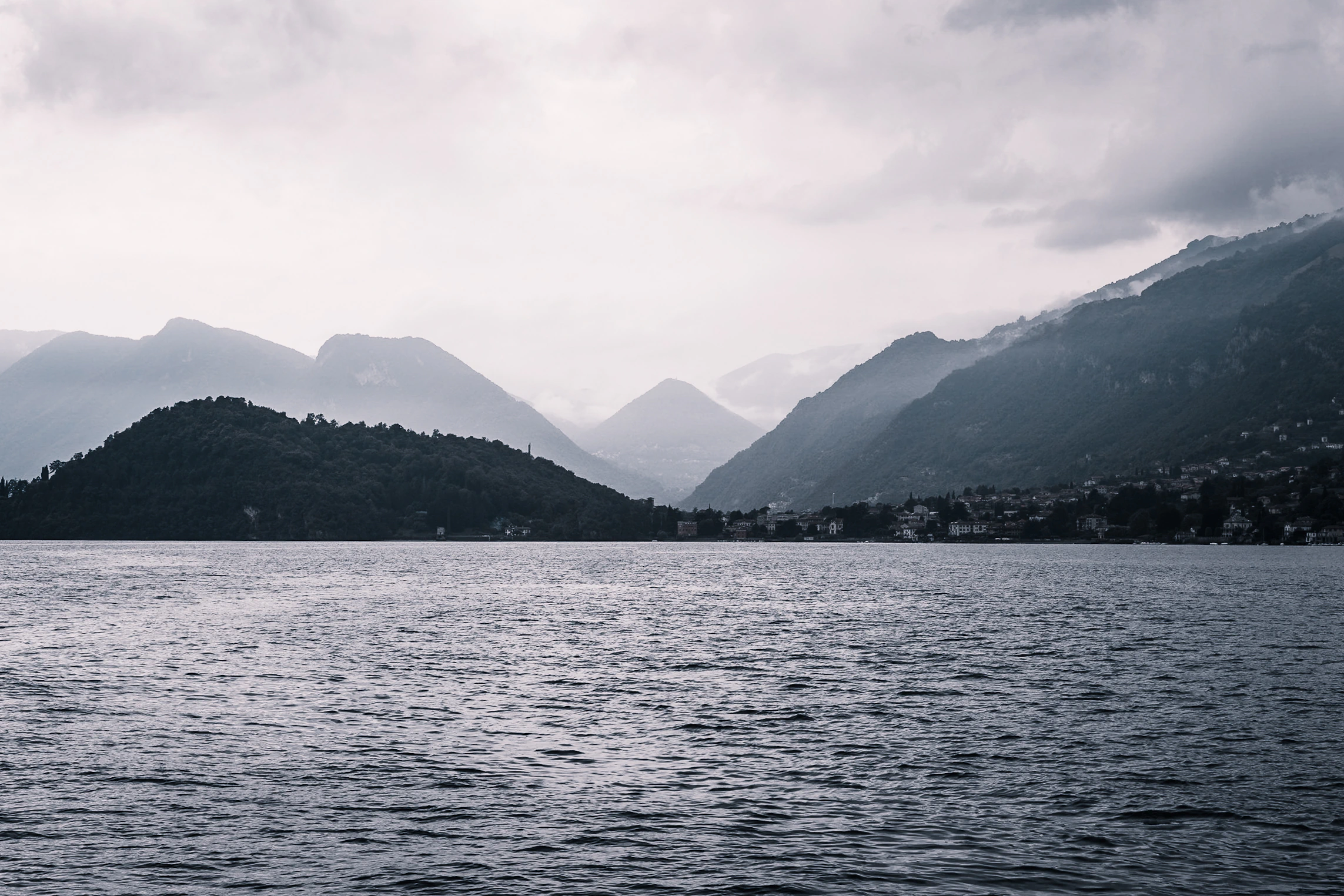 Soft rain light opening above layers of mountains and steel-blue water