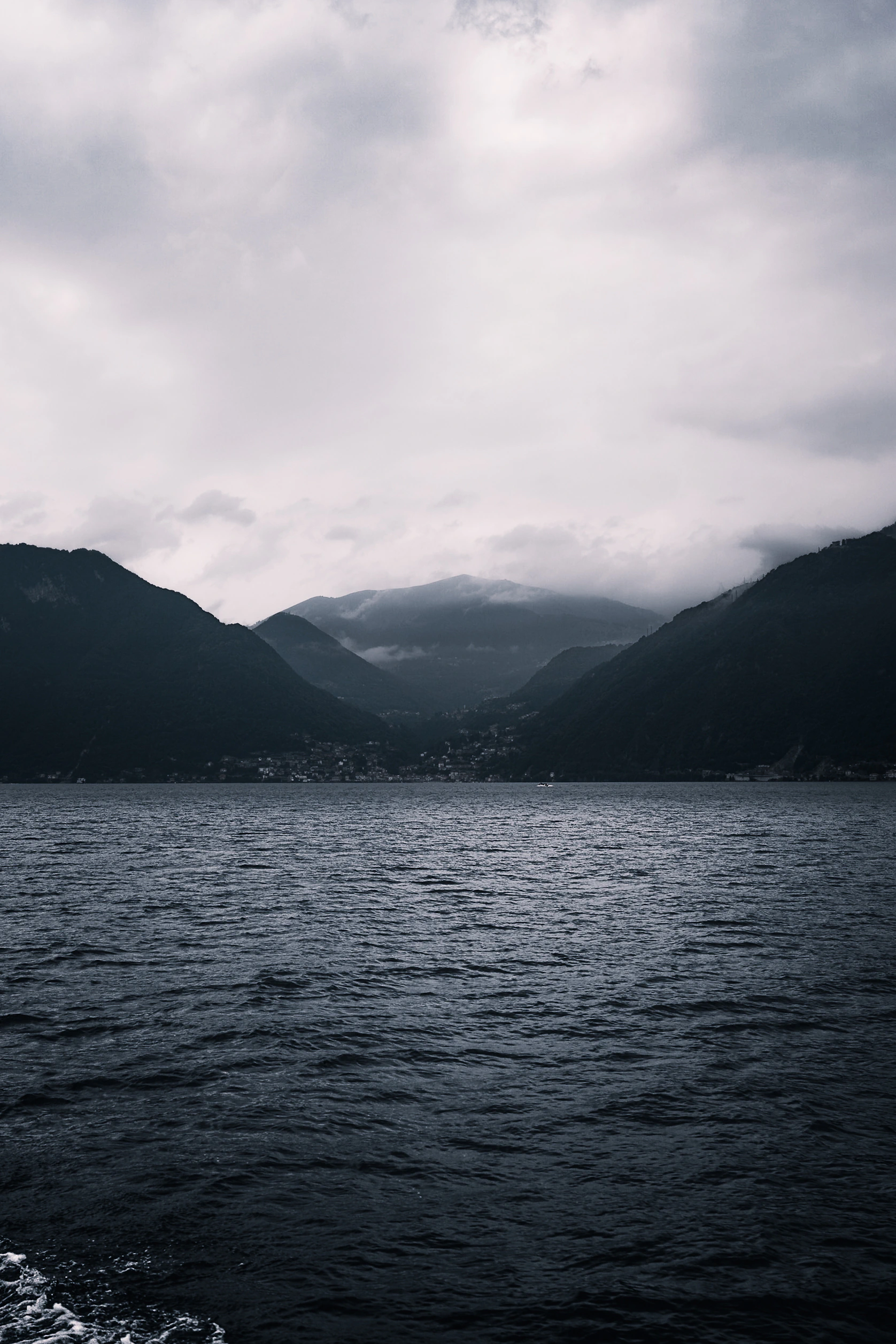 A tall expanse of cloud and dark water framing distant mountain slopes