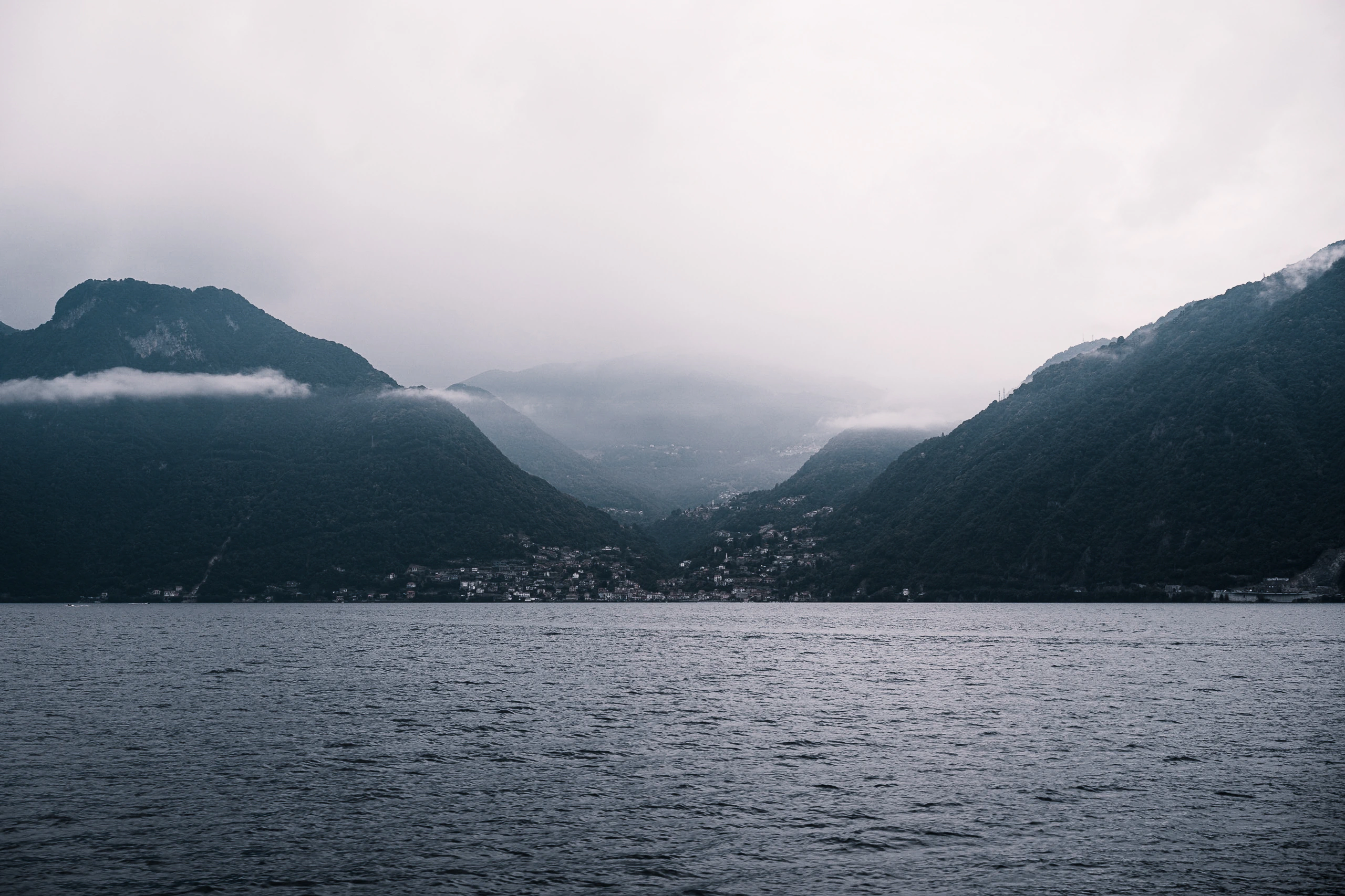 Dark mountain slopes opening towards a distant valley beneath a pale rainy sky