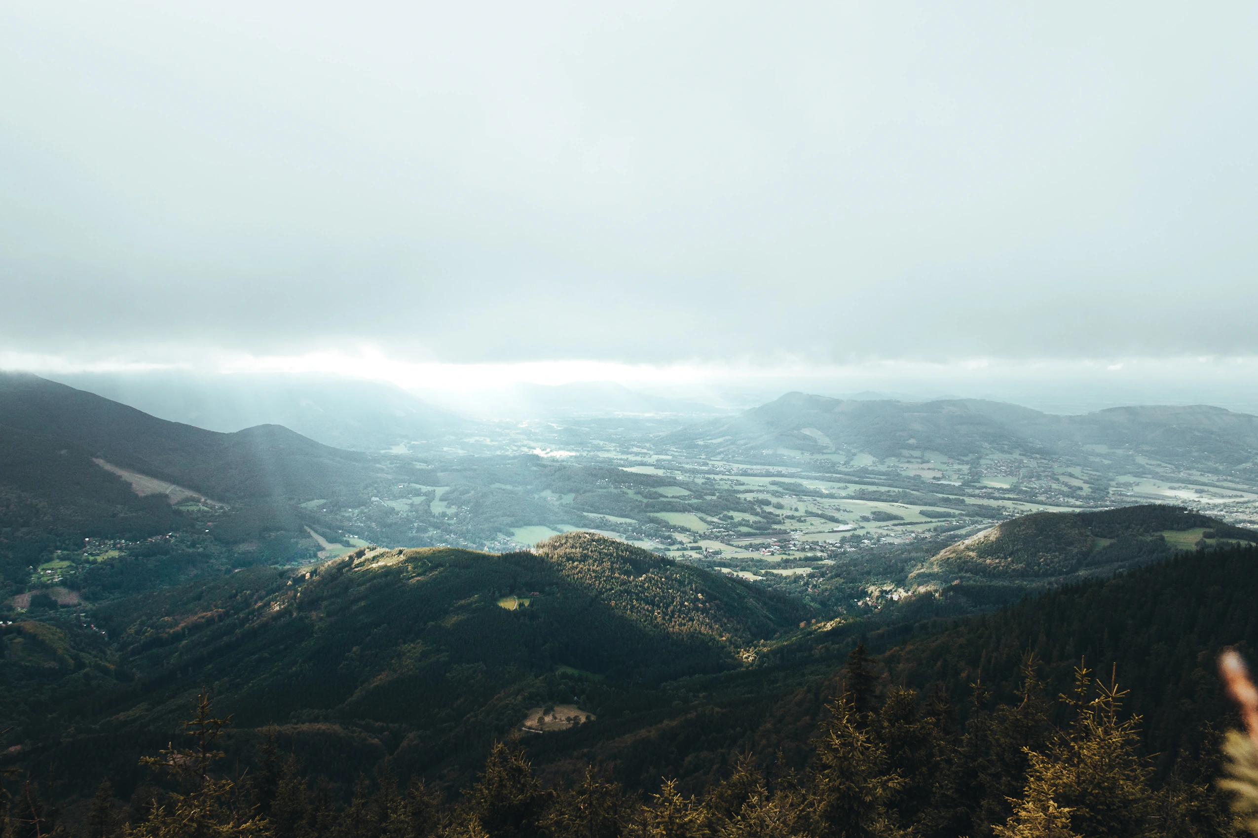 A wide mountain valley beneath low cloud and distant sunlight