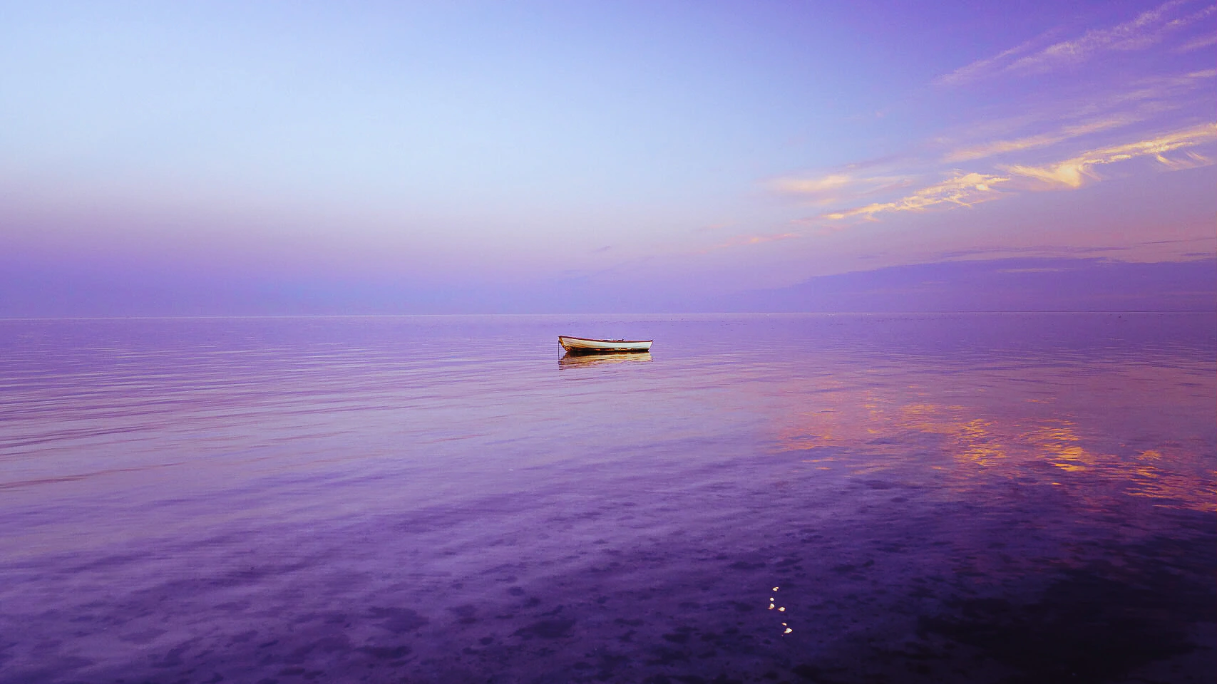 A single boat resting on violet water at dusk