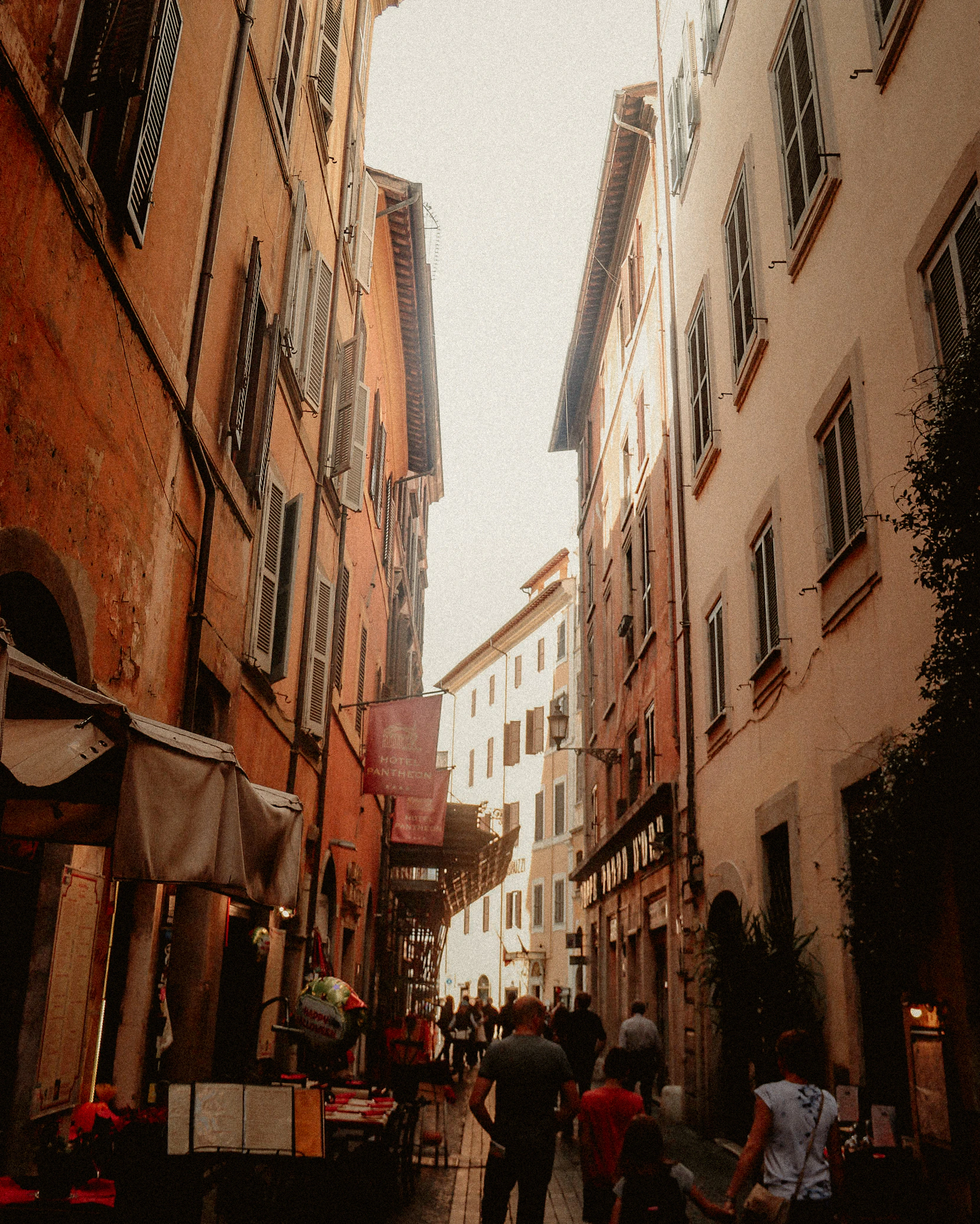 A sunlit narrow street with people passing between tall buildings