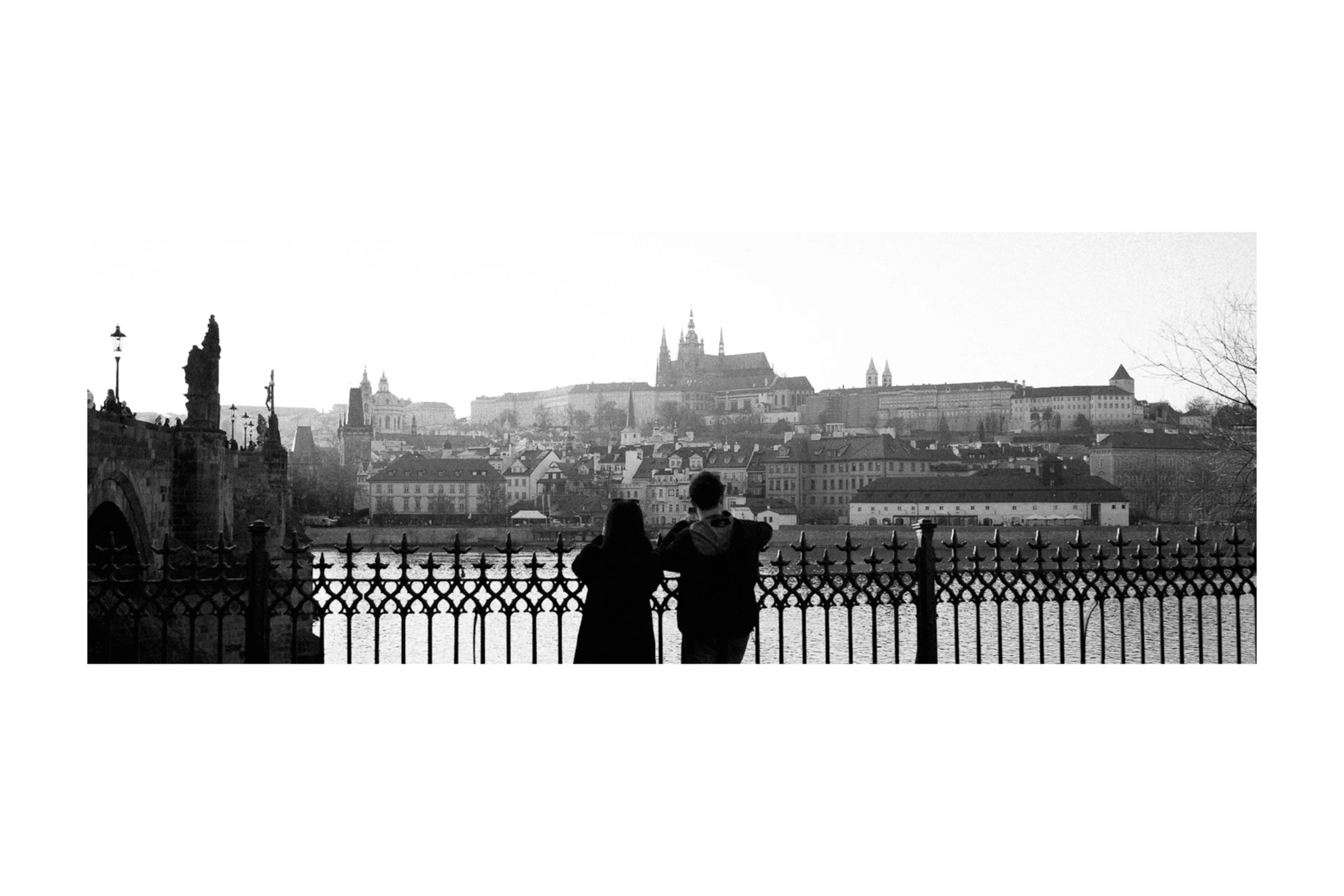 Two people looking across the river toward Prague Castle
