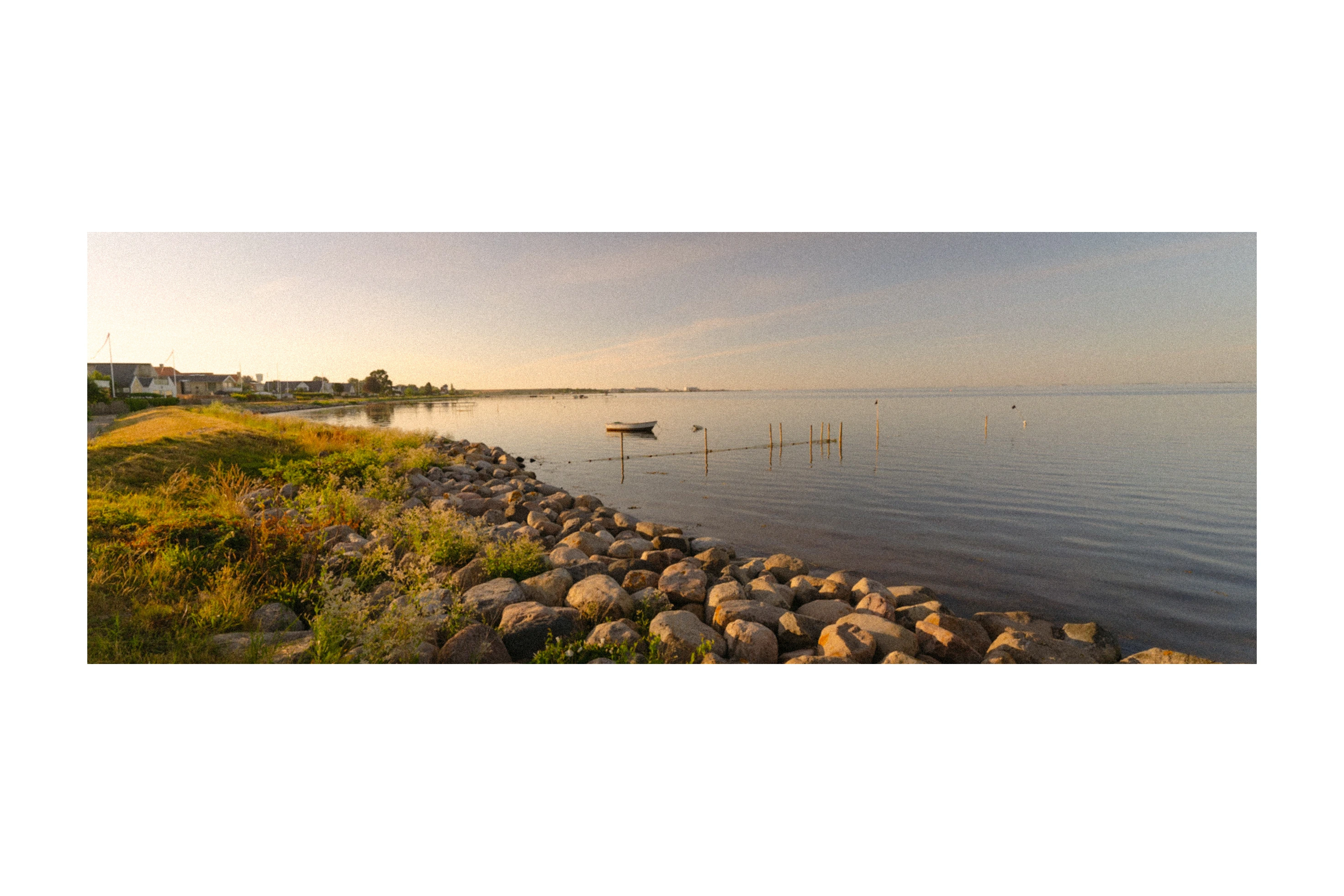 A calm shoreline with rocks and a small boat in warm light